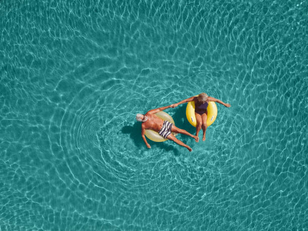 Senior couple enjoy sea water High angle view photo of a senior couple floating in the ocean while using swimming and floating devices inflatable photos stock pictures, royalty-free photos & images