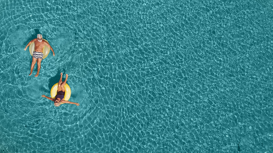 High angle view photo of a senior couple floating in the ocean while using swimming and floating devices; wide photo dimensions