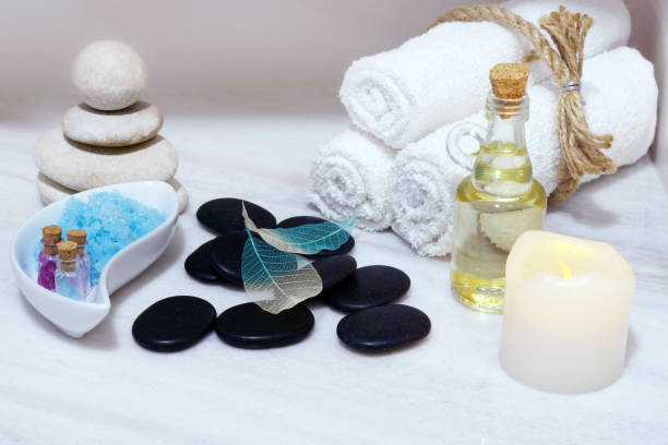 istock Set for spa procedures on a white marble table - aromatic oil, stones for hot massage, blue bath salt and towels, tied with string. 848645954