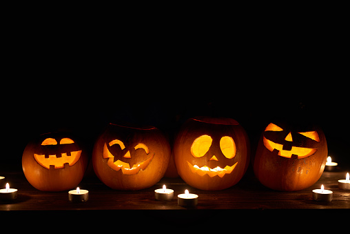 Halloween pumpkins in a row with candles over black background with copy space for text above, front view