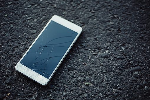Smart phone with broken screen on dark background.
