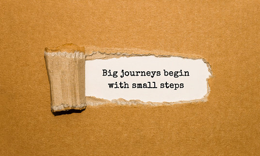 The text Big journeys begin with small steps appearing behind torn brown paper