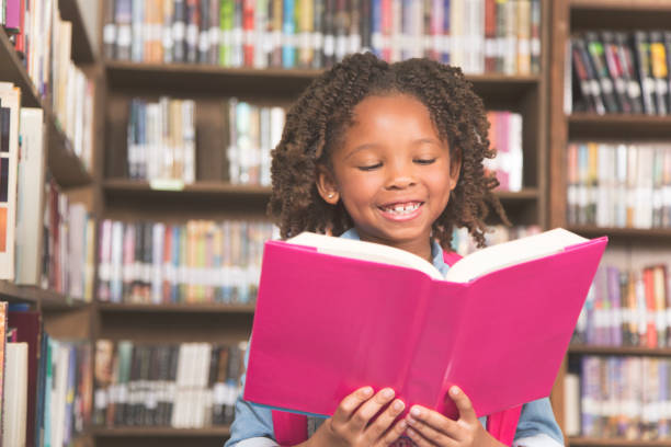 istock African descent little girl in school library reading book. 848744928