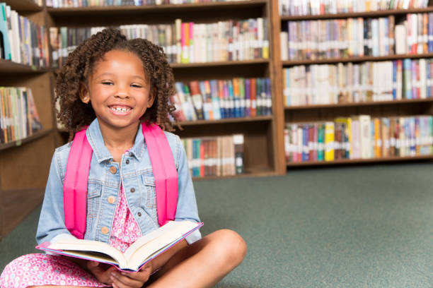 istock African descent little girl in school library reading book. 848745362