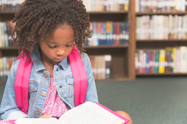 istock African descent little girl in school library reading book. 848745734