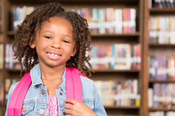 istock African descent little girl in school library with backpack. 848746382