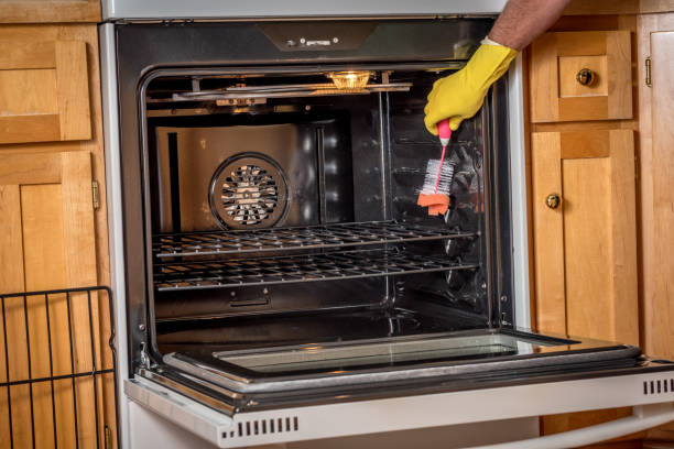 istock Man with yellow glove cleans an oven in the kitchen 848756416