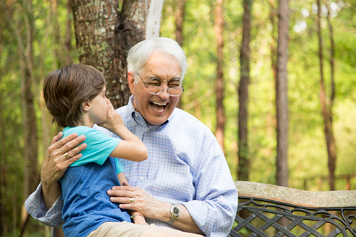 Grandfather and grandson outdoors telling secrets at a park or back yard setting.  Latin and caucasian descent family.