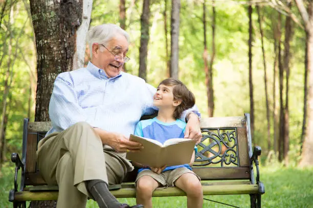 Photo of Grandfather and grandson reading books outdoors together.