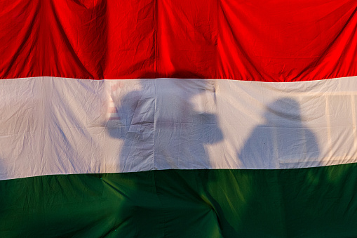 The shadow of the family against the background of a large Hungarian flag in the evening sunlight.