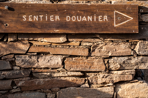 Corsica: a stone wall and the wooden sign of the Sentier des Douaniers (Custom Officers Route), a famous 19 km long coastal path on the Cap Corse