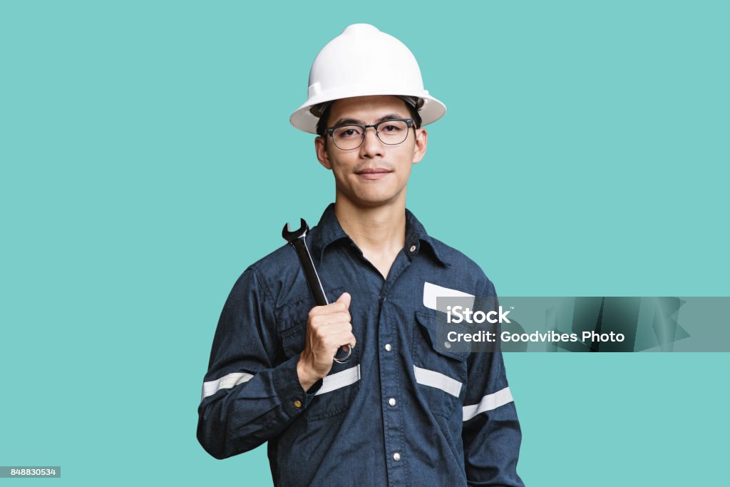 Asian man,Engineer or Technician in white helmet, glasses and blue working shirt suit holding wrench, isolated on green, mechanic and Oil and Gas industrial concept with clipping path. Asian and Indian Ethnicities Stock Photo