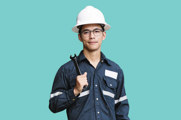 Asian man,Engineer or Technician in white helmet, glasses and blue working shirt suit holding wrench, isolated on green, mechanic and Oil and Gas industrial concept with clipping path. stock photo
