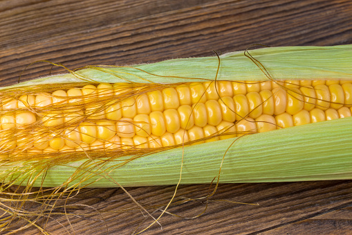 Ripe corncob with fibers on natural wooden background