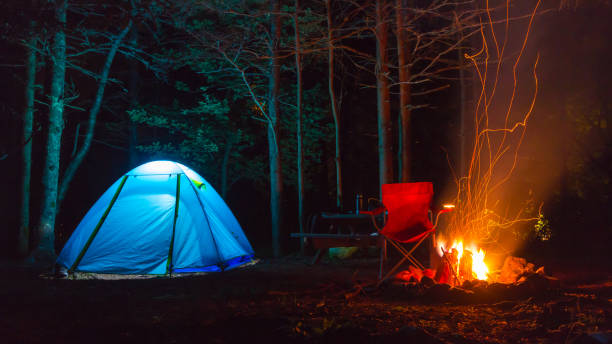 Tent lit up at night with fire pit blue Tent lit up at night with fire pit , chair, and trees all around maine landscape new england sunset stock pictures, royalty-free photos & images