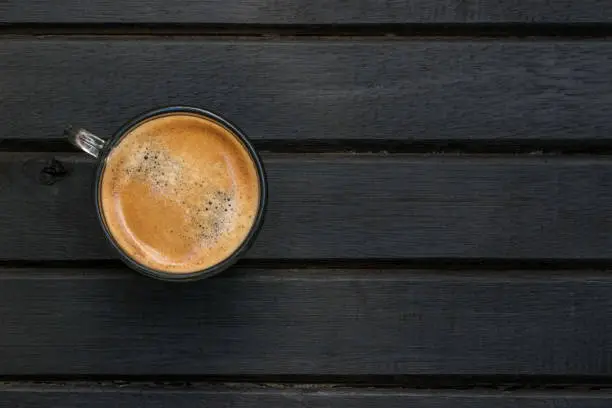 Photo of Fresh brewed espresso coffee on a black wood table, with wood grain, lines, pattern and texture, and copy space to the right