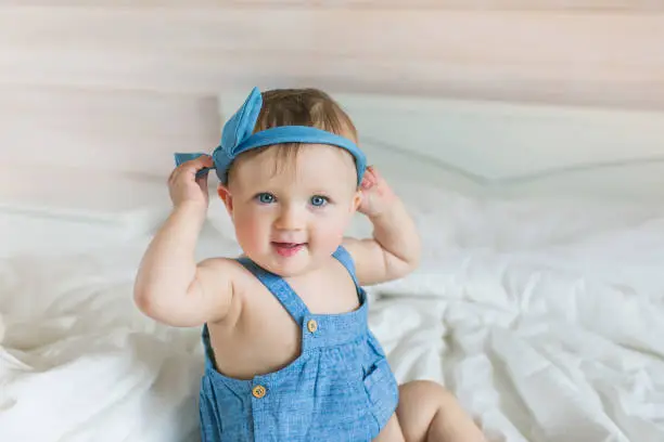 Portrait of a funny little baby in a denim dress on a bed