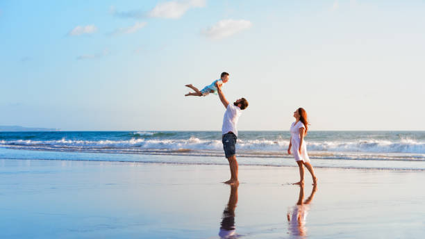 familia - padre, madre, bebé caminar en la playa al atardecer - family beach vacations travel fotografías e imágenes de stock