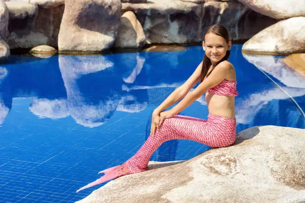 Mermaid girl with pink tail on rock at poolside. Fun, fashion concept. Text space