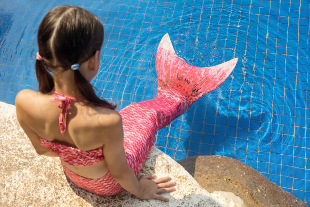 Mermaid girl with pink tail on rock at poolside put feet in water stock photo