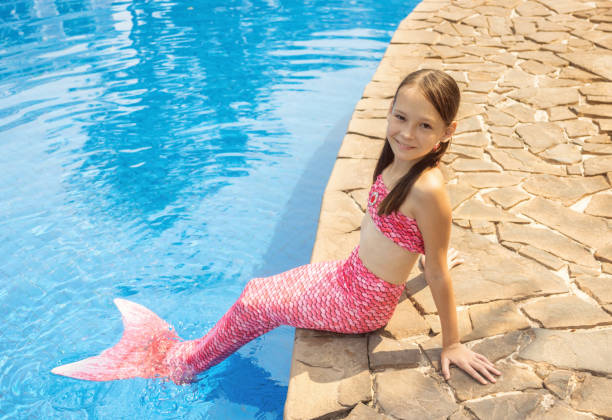 Mermaid girl with pink tail on rock at poolside put feet in water. Top view stock photo