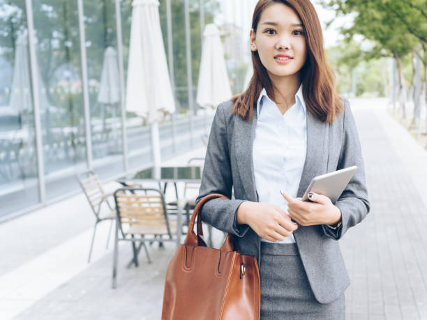 istock pretty asian girl walking outside office building with holding tablet PC 849098420