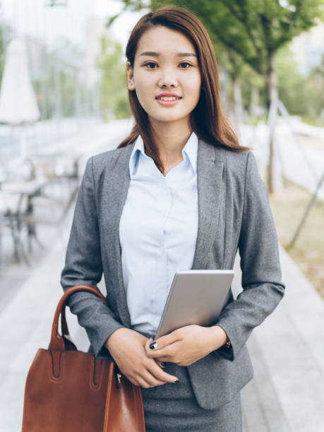 istock pretty asian girl walking outside office building with holding tablet PC 849098612
