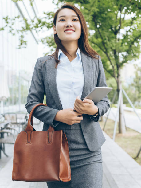 istock pretty asian girl walking outside office building with holding tablet PC 849098666