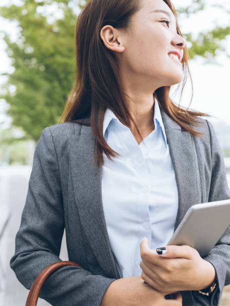 istock pretty asian girl walking outside office building with holding tablet PC 849098778