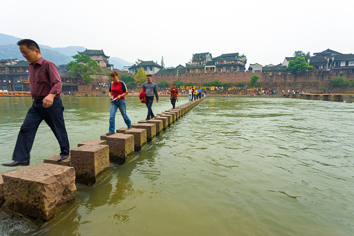 Chinese tourists crossing the stepping stone bridge across the Tuojiang River at the beautiful traditional village and tourist destination of Fenghuang
