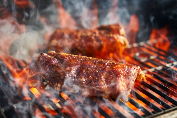bbq pork ribs cooking on flaming grill bbq pork ribs cooking on flaming grill shot with selective focus smoked food stock pictures, royalty-free photos & images
