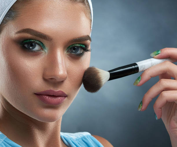 Pretty woman with green makeup drawing blush for herself.