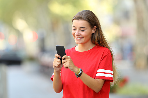 Single happy teen texting on a mobile phone standing on the street