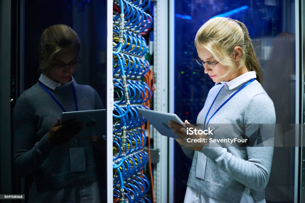 Young Woman Working with Supercomputer Portrait of young smiling woman checking data on digital tablet while working with supercomputer in research center Technology Stock Photo
