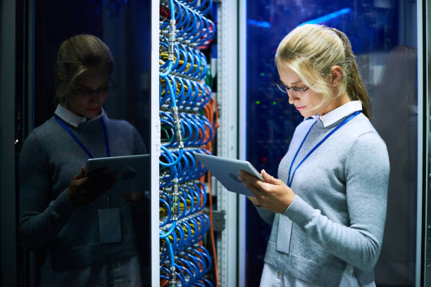 Young Woman Working with Supercomputer Portrait of young smiling woman checking data on digital tablet while working with supercomputer in research center data cable stock pictures, royalty-free photos & images