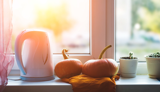 Pumpkins on the windowsill, a kettle on the window background, autumn background. banner for Halloween or Thanksgiving