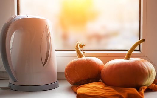 Pumpkins on the windowsill, a kettle on the window background, autumn background. banner for Halloween or Thanksgiving