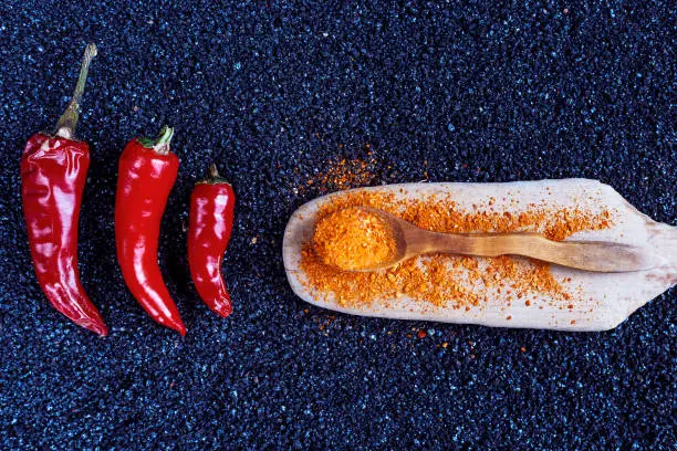 Red chili pepper, fresh and ground on darkly blue background, top view. 3 pepper, lie in a row