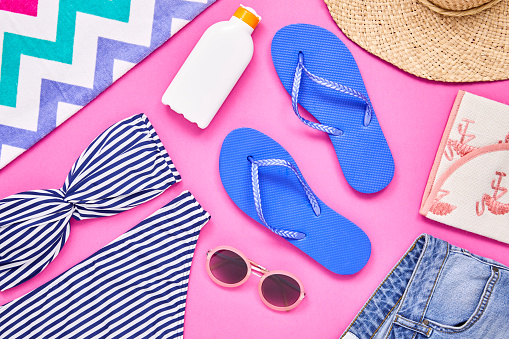 Overhead colour block shot of summer vacation accessories. Flat lay of travel and beach equipment. They are arranged on pink background.