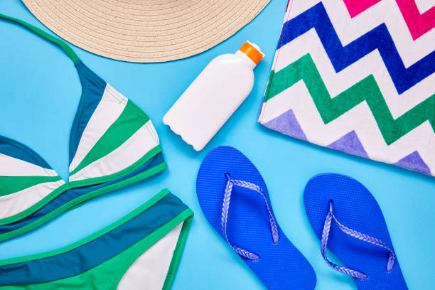 Flat lay shot of summer vacation accessories over blue background Flat lay shot of summer vacation accessories. Overhead shot of sun hat flip-flop suntan lotion beach towel and bikini. They are color blocked and arranged on blue background. swimwear bikini top bikini bikini bottom stock pictures, royalty-free photos & images