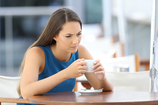 Single angry woman thinking and holding a cup sitting in a bar terrace