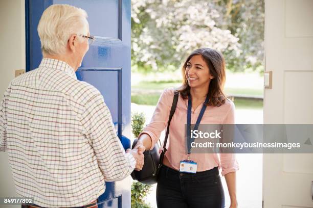 Senior Man Greeting Young Woman Making Home Visit Stock Photo - Download Image Now - Community Outreach, Senior Adult, Opening