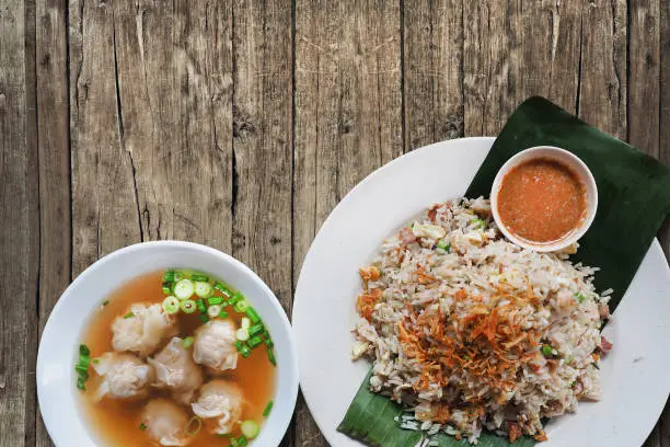 Set menu Traditional local fried rice with spicy dip and wonton soup in Malaysia and Singapore served on white dish with banana leaf on wooden table background and leave for copy text space