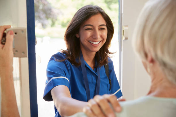istock Nurse on home visit greets senior woman, over shoulder view 849178158