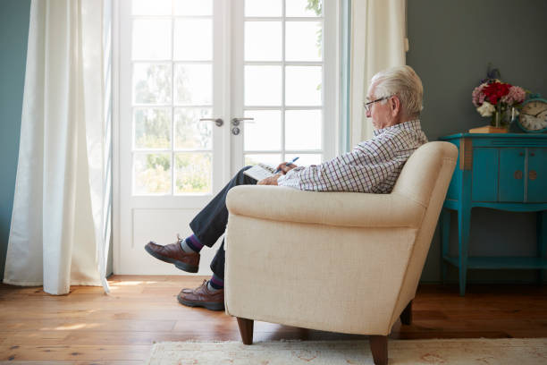 istock Senior man sitting in an armchair doing  crossword, side view 849178490