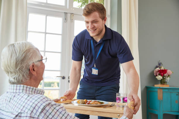 travailleur de soins masculins qui dessert dîner à un homme senior à son domicile - profession médico sociale photos et images de collection