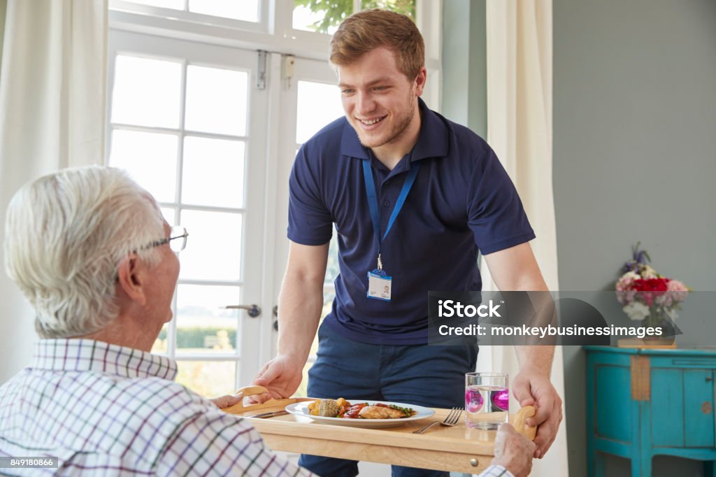 Male care worker serving dinner to a senior man at his home Community Outreach Stock Photo