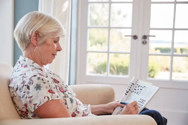 Senior woman sitting in armchair doing  a crossword at home