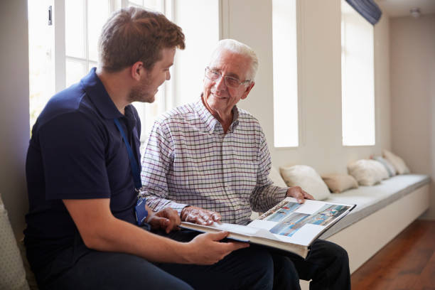 ältere mann sitzt mit krankenpfleger fotoalbum betrachten - altersheim fotos stock-fotos und bilder