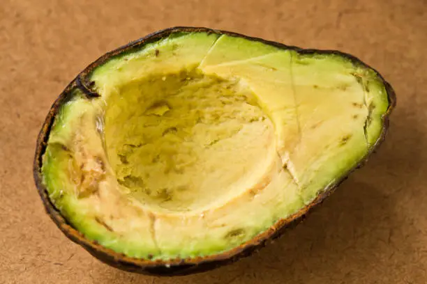 An avocado pear has been sliced in half, only to find that the inside is overripe and inedible.